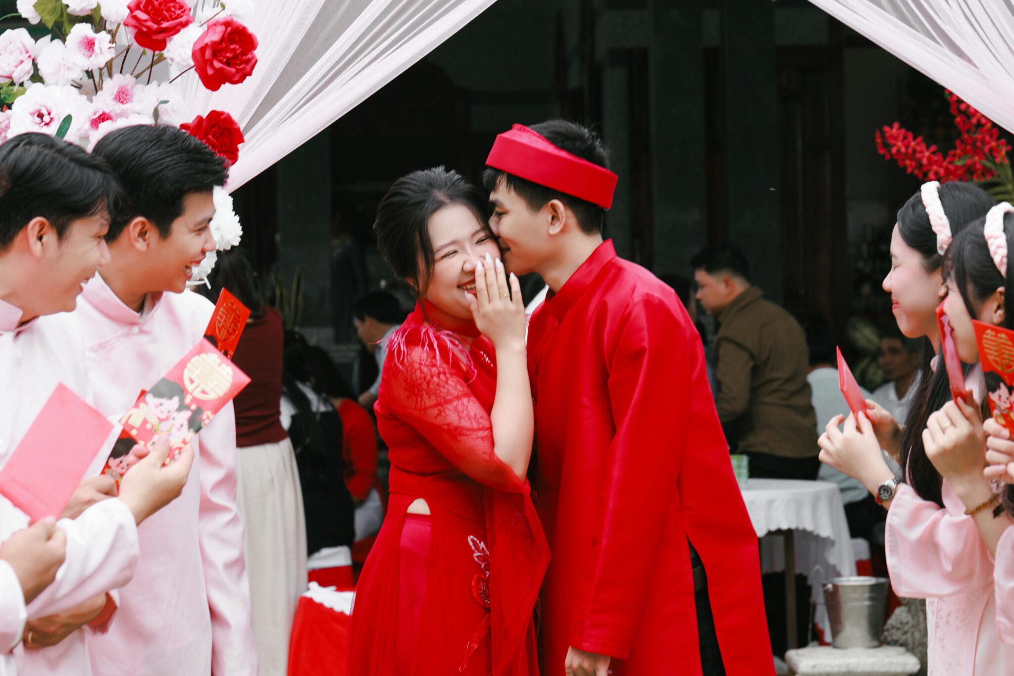 Newlyweds with guests holding red envelopes around them.